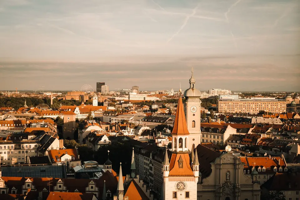 Luftaufnahme von München, die historische Gebäude und eine lebendige Stadtlandschaft zur Sonnenuntergang zeigt.